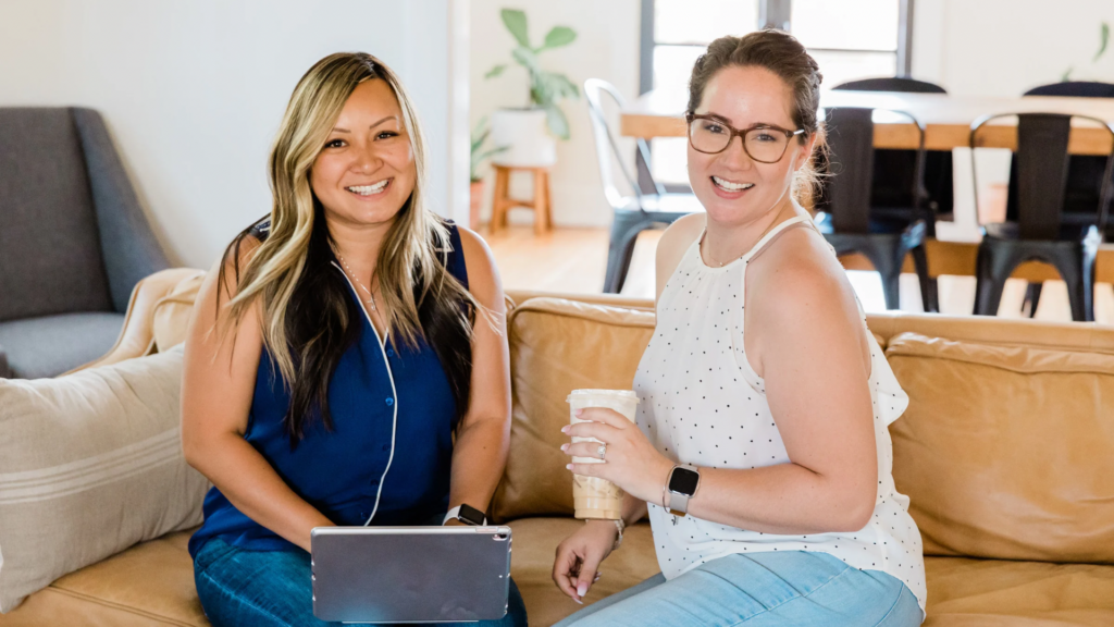 A diverse group of women in tech working together in a modern office, with one woman balancing a laptop and a baby, representing work-life balance.