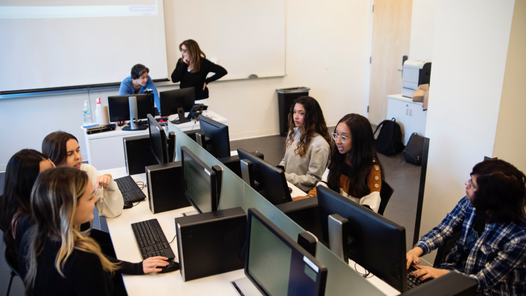 A diverse group of women working together on laptops in a modern tech office, representing collaboration and support for women starting careers in tech.